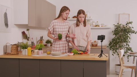 PAN shot of twin girls cooking in kitchen and recording video for their video blog