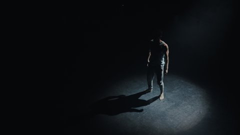 Handsome Young Isolated Ethnic Dancer Standing and Warming Up In The Middle Of The Empty Theatre Room With Spotlight On Him. Jumping and Walking Around, Preparing For the Dance Class Choreography.