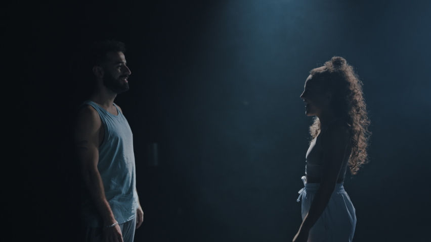 Isolated Beautiful Interracial Couple Standing Alone In the Middle of an Empty and Dark Theatre Building, Looking At Each Other Before Putting Hands Together, Laughing and Teasing Each Other.