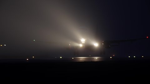 Night airport with light on the runway on which the plane travels and takes off. Foggy weather and the light of an airplane taking off into the sky.