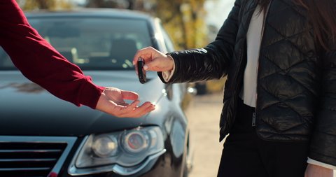 Man gets the car key from seller - satisfied - trade closed - new car in the background. Concept of buying a vehicle, auto business.