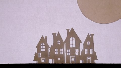 Puppet Shadow Theatre. Santa Claus on a sleigh with reindeer flies from the big moon to earth over houses with glowing windows
