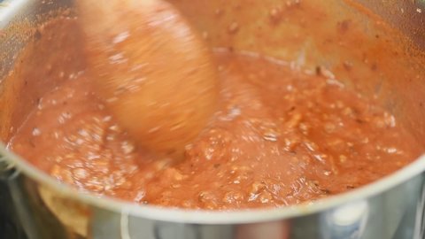 Tomato sauce with mince is boiling and stirring in a pot.