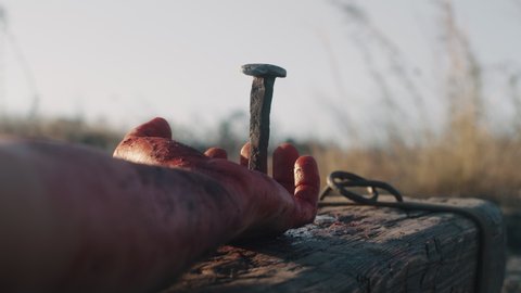 Crop man roman warrior hitting metal nail with hammer while crucifying Jesus Christ on cross in daytime