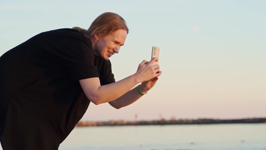 a woman in a black tunic takes a photo or video of someone on her smartphone by the sea. photo in memory of the vacation.