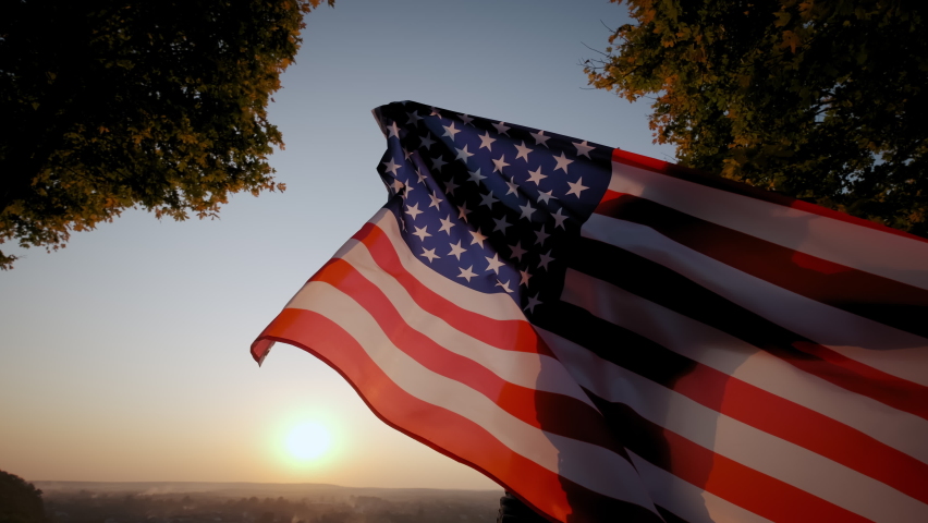 Back view of happy woman with USA national flag standing outdoors at sunset. Close up