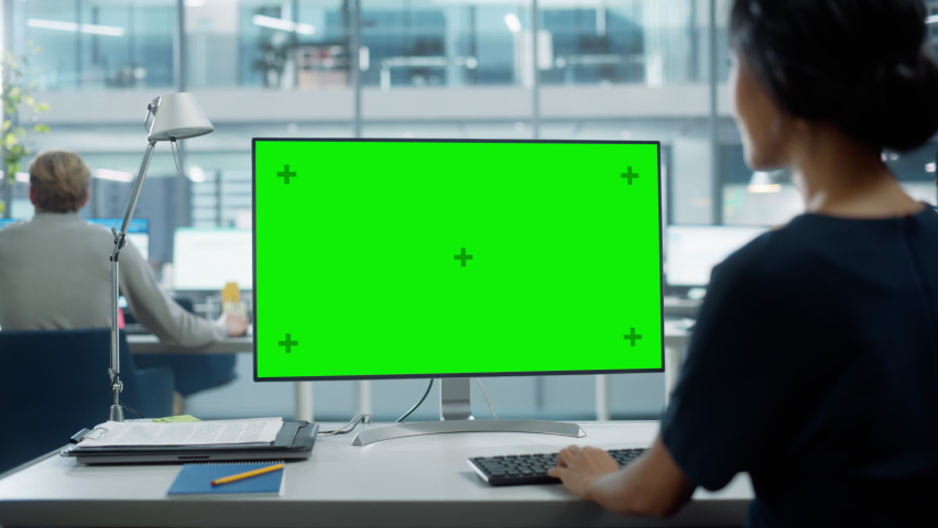 Close Up Over the Shoulder Shot of a Businesswoman Working on Desktop Computer with Chroma Key Green Screen Mock Up Display. Digital Projects Manager Typing Data, Using Keyboard and Mouse. Royalty-Free Stock Footage #1082416573