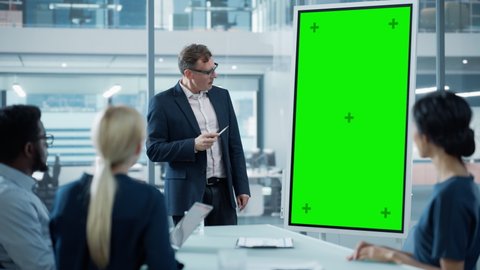 Company Operations Manager Holds Meeting Presentation for a Team of Economists. Adult Male Uses Digital Whiteboard with Vertical Green Screen Mock Up Display. People Work in Business Office.