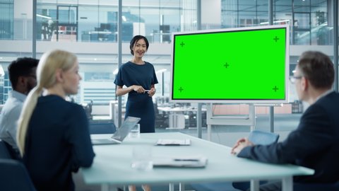 Female Operations Manager Holds Meeting Presentation for a Team of Economists. Asian Woman Uses Digital Whiteboard with Horizontal Green Screen Mock Up Display. People Work in Business Office.