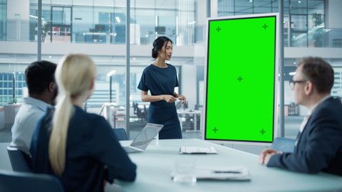Female Operations Manager Holds Meeting Presentation for a Team of Economists. Asian Woman Uses Digital Whiteboard with Vertical Green Screen Mock Up Display. People Work in Business Office.