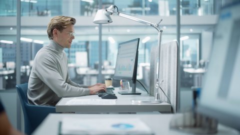 Big Diverse Corporate Office: Portrait of Handsome Manager Using Desktop Computer, Businessman Managing Company Operations, Analysing Statistics, Commerce Data, Marketing Plans. Zoom In Shift Focus.