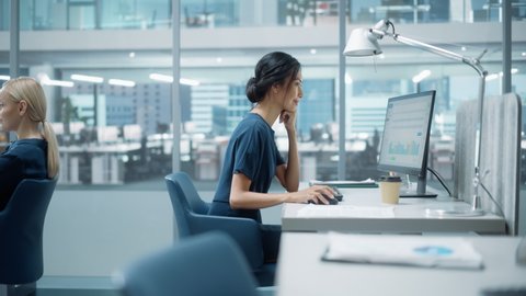 In Big Corporate Office: Beautiful Asian Business Manager Using Computer, Businesspeople and Experts Working Around Her, Analysing Statistics, Commerce Data, Marketing Plans. Zoom In Portrait.
