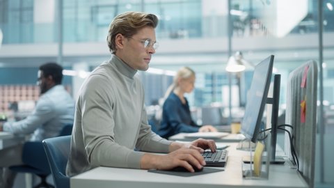 In Big Corporate Office: Portrait of Confident Handsome Manager in Grey Turtleneck Using Computer, Businesspeople and Experts Working Around Him, Analysing Statistics, Commerce Data, Marketing Plans.