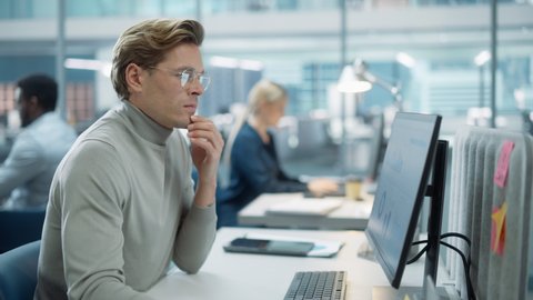 In Big Corporate Office: Portrait of Confident Handsome Manager in Grey Turtleneck Using Computer, Businesspeople and Experts Working Around Him, Analysing Statistics, Commerce Data, Marketing Plans.
