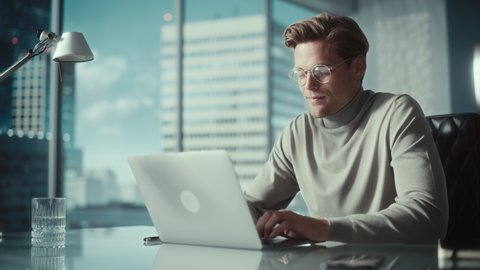 Creative Businessman in a Turtleneck Jumper Sitting in Modern Office, Using Laptop Computer Next to Window with Big City with Skyscrapers View. Successful Finance Manager Planning Work Projects.