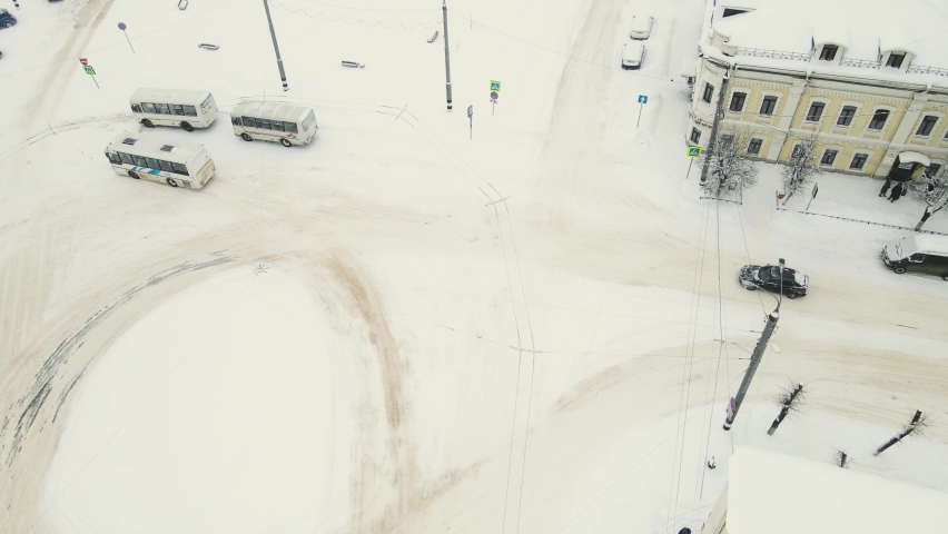 On a snow-covered city road, after a blizzard, a bus and a car are going. Aerial view of the roadway and passing vehicles. Sudden precipitation, sharp climate change. UHD 4K