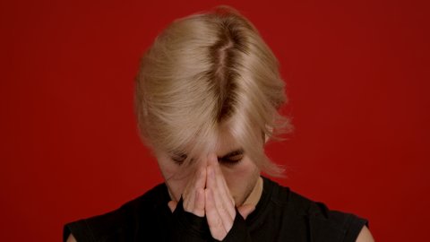 Getting ready to fight. Close up portrait of concentrated young blonde kickboxer breathing and praying, looking sullenly at camera, red studio background, slow motion