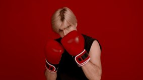 Challenge accepted. Young aggressive man kickboxer wearing boxing gloves tapping hands, looking at camera, ready to fight over red studio background, slow motion - Powered by Shutterstock - Get 15% off with code: PIKWIZARD15