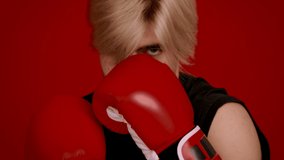 Boxing punch. Close up portrait of young sporty professional fighter wearing boxing gloves doing punch forward to camera, red studio background, slow motion - Powered by Shutterstock - Get 15% off with code: PIKWIZARD15