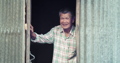 An Asian man who is more than seventy years old and works as a wage earner in a farm, live in a poor house. The lid and roof are galvanized sheet, opening the door smiling
