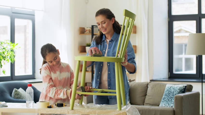 Furniture renovation, diy and home improvement concept - happy smiling mother and daughter sanding old round wooden chair with sponge at home