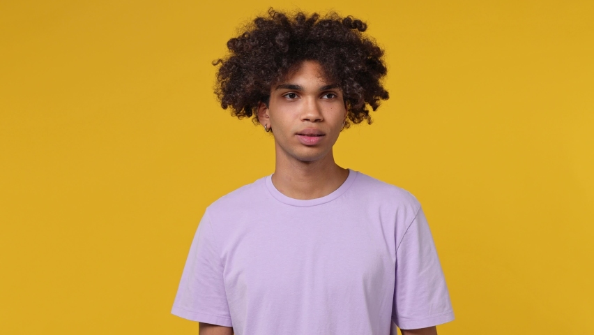 Smiling young curly african american man 20s wears white t-shirt dance clenching fists waving rising gesticulating hands have fun enjoy celebrate isolated on plain yellow background studio portrait Royalty-Free Stock Footage #1082429980