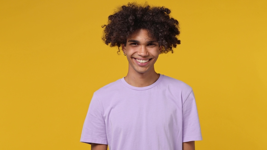 Attractive excited happy vivid young curly african american man 20s wears white t-shirt looking camera smiling isolated on plain yellow background studio portrait. People emotions lifestyle concept