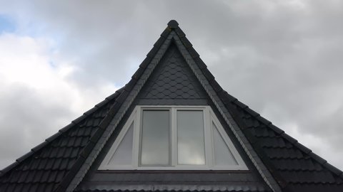 Time-lapse shot of clouds reflected in windows of residential house roof with black tiles.