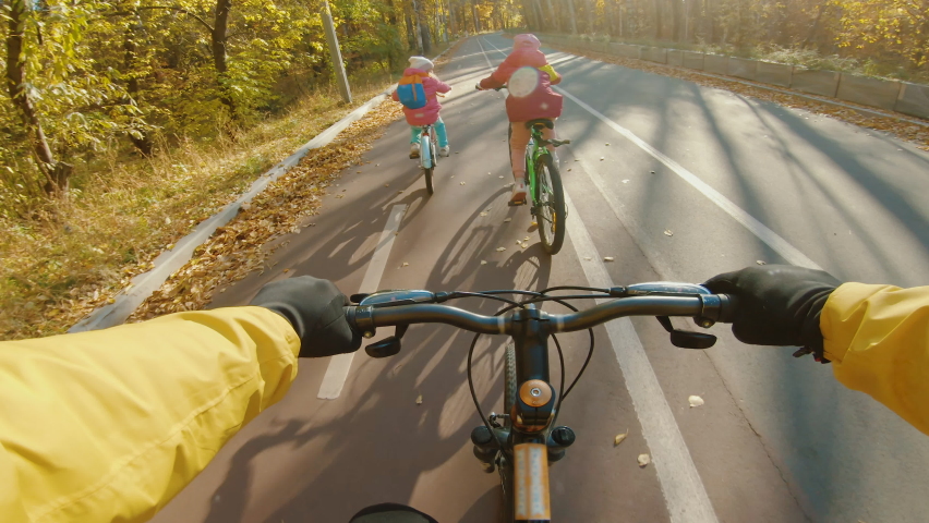 Father with her daughters have a bike ride in autumn park, POV view. Two little girls riding bicycle on bike path, family walk at beautiful sunny day, happy childhood Royalty-Free Stock Footage #1082434003