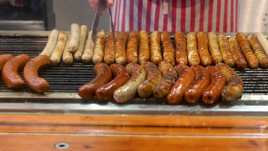 Grilling sausages on Christmas market. Man preparing Sausages on barbecue grill. Bratwurst on BBC. Sausage roasted on coals. Traditional street food in Germany.