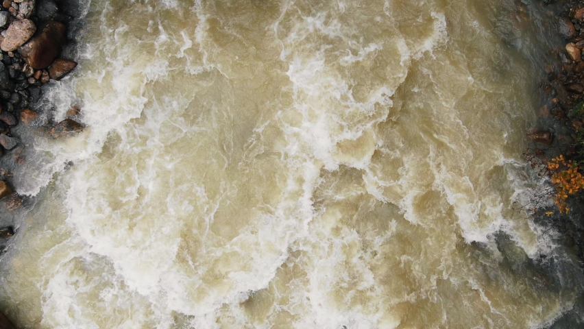 Young woman tourist lies on wooden river footbridge with rough water streams connecting rocky and forestry banks, aerial view