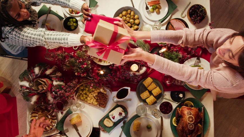 Friends giving presents to each other top view, celebrating new year, sitting at dining table. International young people making surprises. Diverse students during christmas party at home.  | Shutterstock HD Video #1082437291