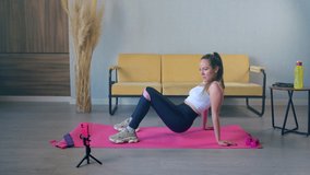Girl does not want to exercise in sports centre, so she using mobile app or video guide to work out at home. Lower body training with resistance band
