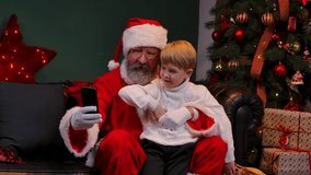Santa Claus with a child sitting on his lap are taking a selfie using a smartphone. Concept of the New Year spirit, holidays and celebrations. Close up. Slow motion. - Powered by Shutterstock - Get 15% off with code: PIKWIZARD15