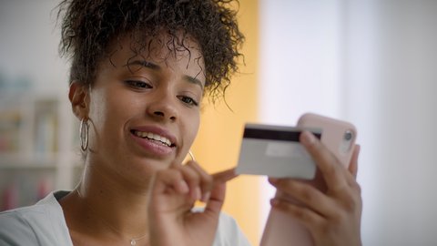 Happy and Smiling African American Woman Making a Card Payment Through Mobile Phone to Pay Bills. Attractive Black Girl Putting Debit or Credit Card Details on a Smartphone or Cellphone to Make Online