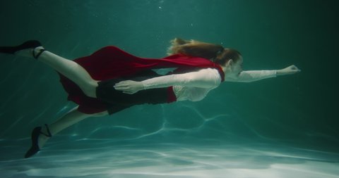Cinematic slow motion, beautiful superhero business woman with red cape swims underwater reaching to help slow motion.