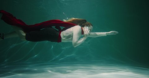 Client support concept. Beautiful young business woman with superhero cape swims underwater talking on phone slow motion