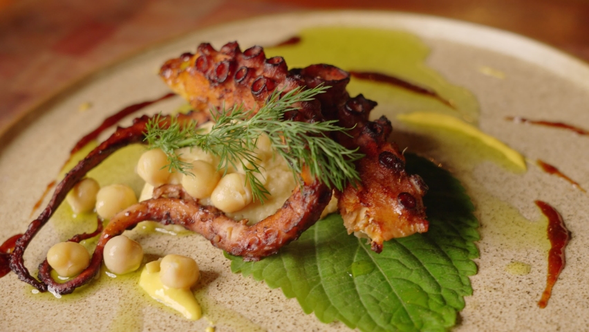Close up slow motion shot of a complete dish of grilled octopus with chickpeas salad, beautifully garnished and plated with aesthetic cooking concept. Royalty-Free Stock Footage #1082445949