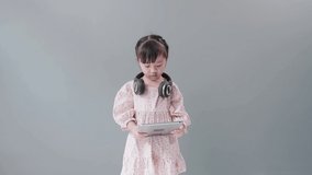 Little Asian girl with headphone enjoy watching video online on tablet and dancing happily.