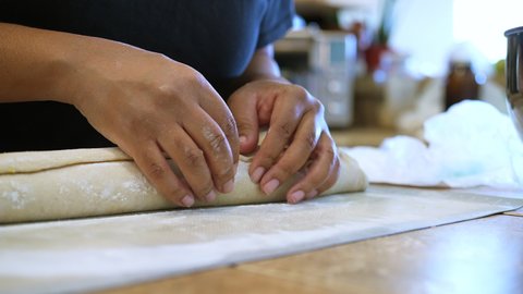 After rolling dough, sugar and cinnamon into a roll, the chef pinches the seam together to press and seal before slicing into rolls