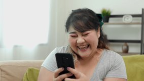 Body positive plus size female holding mobile phone taking selfie photo using smartphone camera. Happy woman plus size video call in living room.