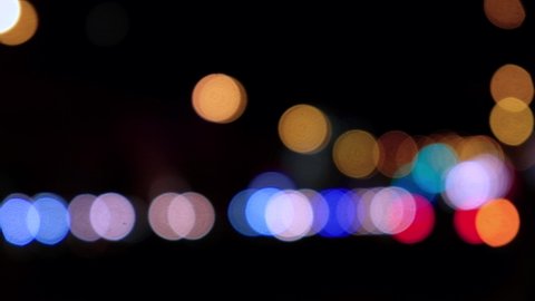 Lights of cars driving in evening city. Defocused headlights and taillights. Moving bokeh circles of cars in night. Blurred city traffic background