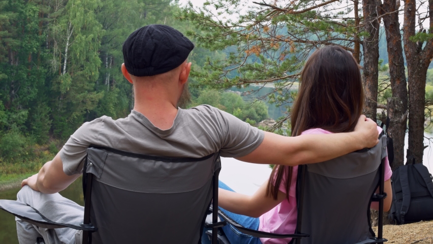 Man and Woman Sit in Nature in the Woods by the Cliff on the River Bank in Folding Camping Chairs. Weekends with the Family on the Hike. Healthy Relationship Between Husband and Wife