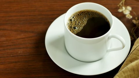 White coffee cup, hot coffee, smoke rising from the coffee cup on a wooden table background.