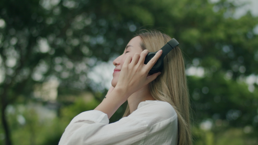 Asian woman enjoy the breeze outdoors and have fun wearing headphones listening to music in nature breathing fresh air.