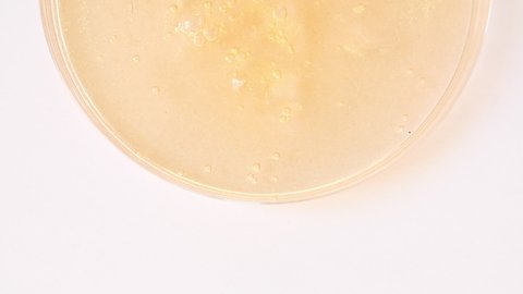 Yellow Transparent Cosmetic Gel Cream With Molecule Bubbles Flowing On The Plain White Surface. Macro Shot