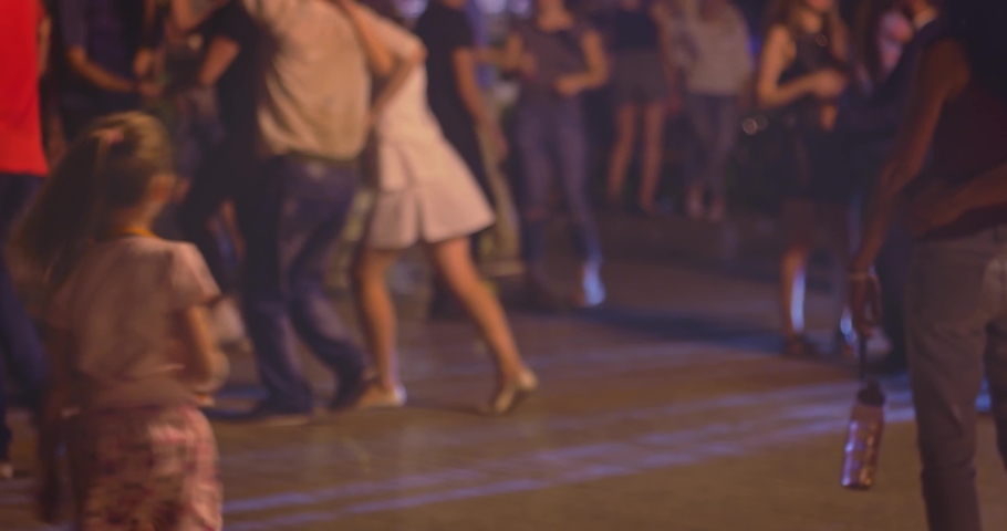 Many couples dancing latin-american dances outside little girl trying to do the same dance moves in foreground. Street salsa dance in the night, many young couples dance social Latino dances defocused | Shutterstock HD Video #1082458366