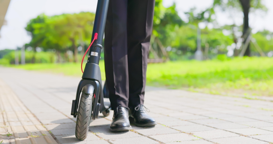 asian businessman standing with electric scooter is using mobile phone while commuting in the city