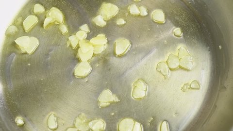 Cooking and stirring of sliced garlic in a frying pan.