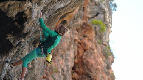 strong female rock climber climbs up hard tough challenging rock route on overhanging black crag. mountain and rock climbing outdoors